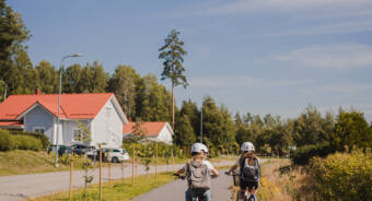 Två barn cyklar på cykelvägen. Barnen har vita hjälmar och ryggsäckar på ryggen.