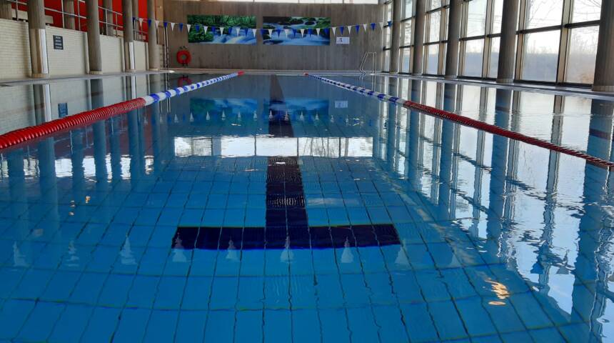 Uimahallin uima-allas jossa on sinertävää vettä, jonka oikealla puolella on suuret ja korkeat ikkunat koko seinän pituudelta.