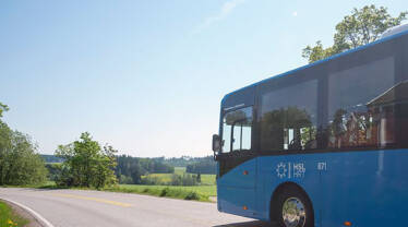 HSL:n sininen bussi maalaismaisemassa aurinkoisella kesäsäällä.