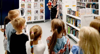Esikoululaisia kirjastovierailulla, kirjastonhoitajalla Mikki Hiiri -pehmohahmo kädessä.