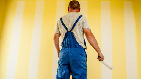 En målare står framför en vägg som målats gul med ljusa ränder.