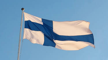 Kuvassa Suomen lippu liehuu sinistä taivasta vasten.