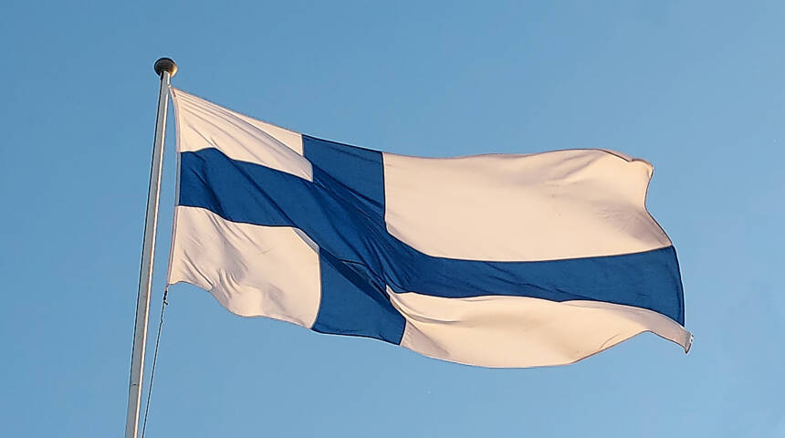 Kuvassa Suomen lippu liehuu sinistä taivasta vasten.