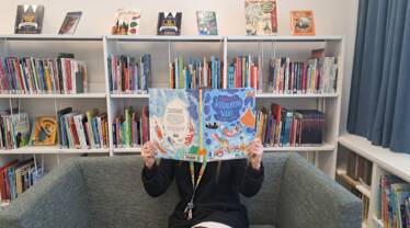 nainen istuu sohvalla ja lukee lasten kuvakirjaa kirjastossa