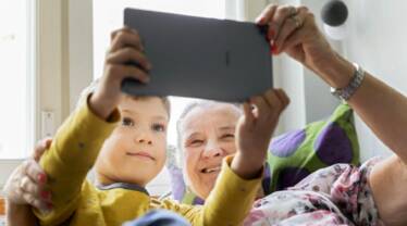 Poika ja mummi käyttävät e-kirjastoa tabletilla sohvalla maaten.